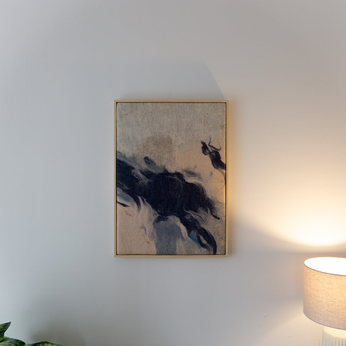 Wandkleed What time leaves behind 01 in een lichte houten baklijst aan een lichte wand, naast een brandende tafellamp.