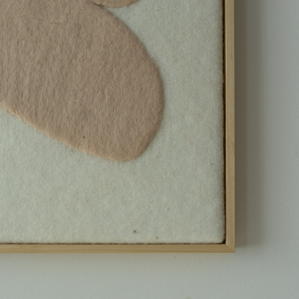 Detail van het vilten Stone wandkleed met zachte beige vorm en houten baklijst.