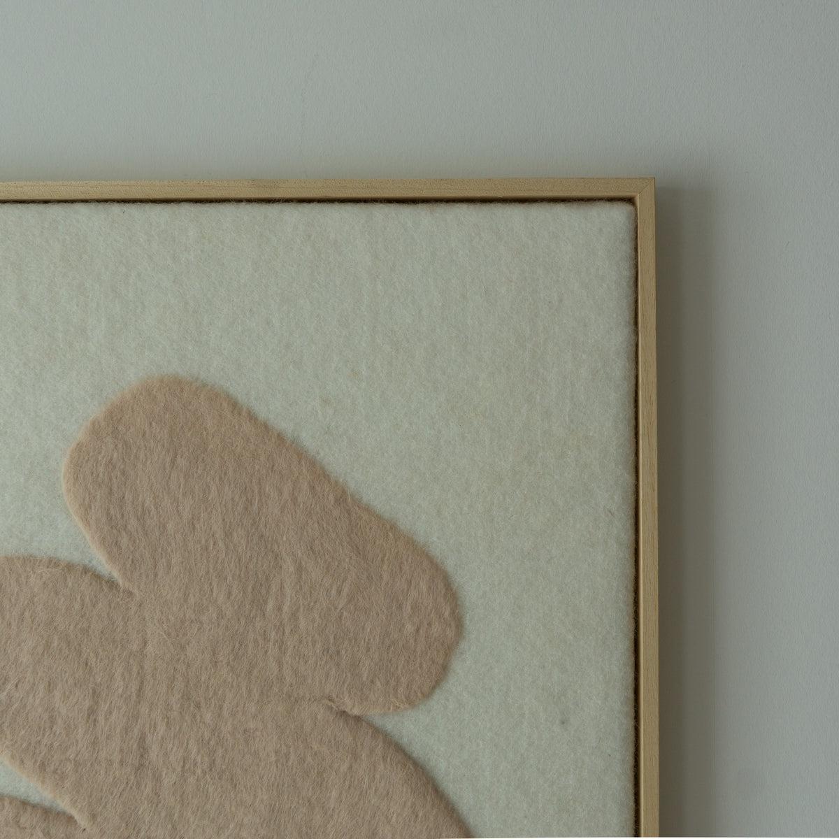 Close-up van het wollen wandkleed met lichte ondergrond, beige vorm en houten baklijst.