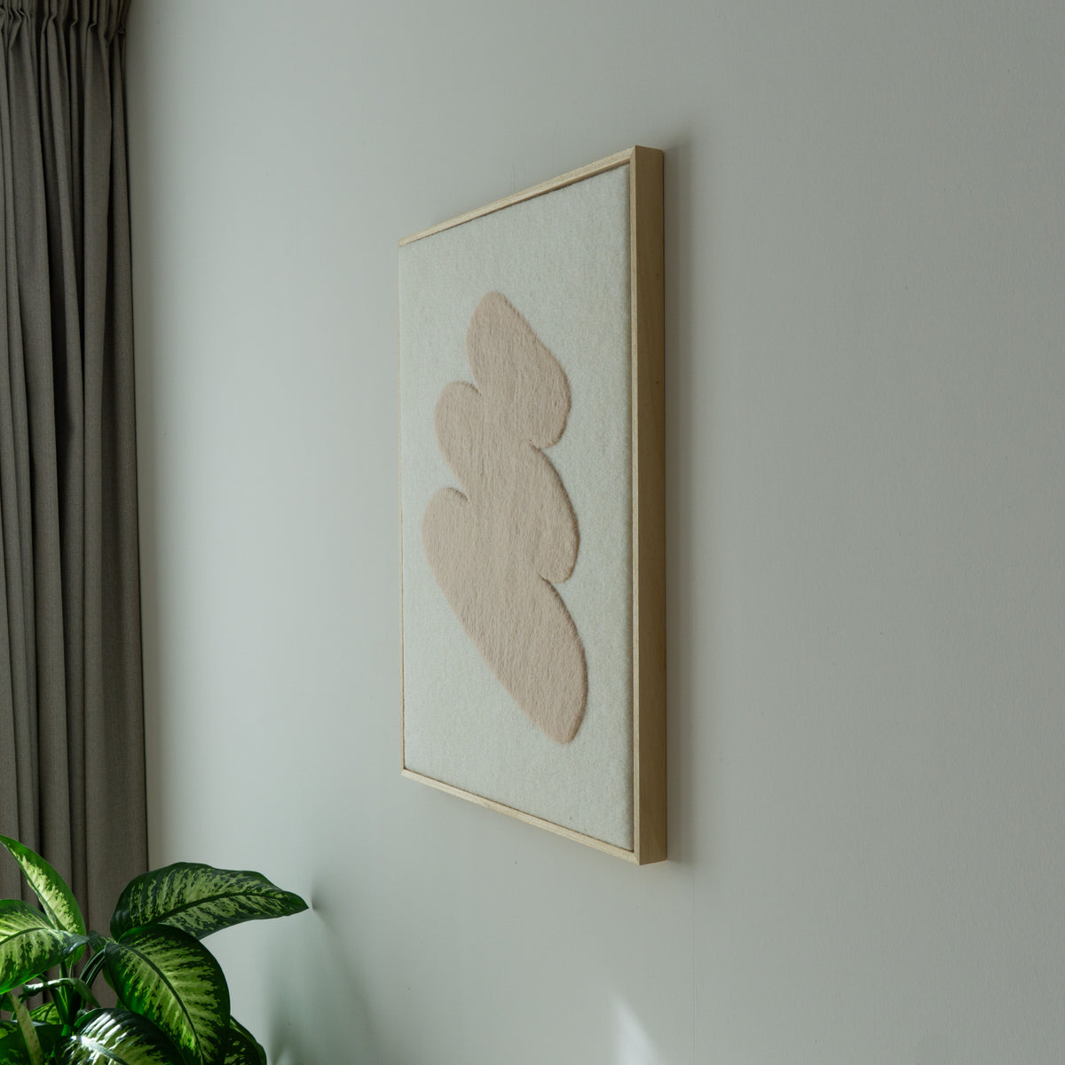 Zijaanzicht van het vilten Stone wandkleed in een lichte houten baklijst.