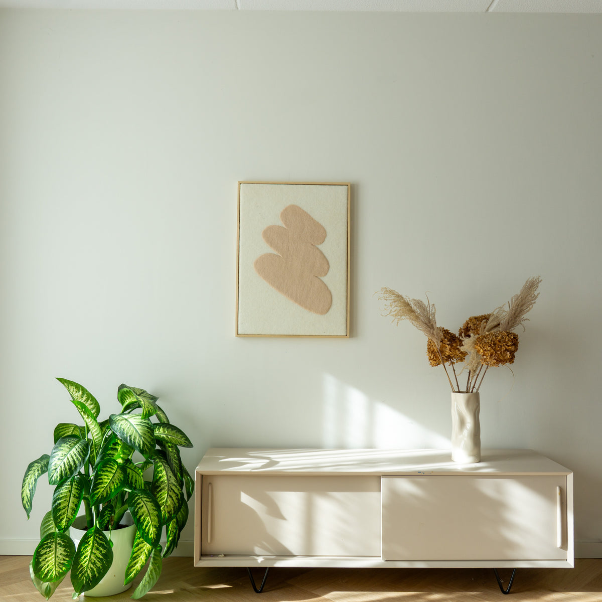 Wollen Stone wandkleed in een licht interieur met natuurlijke kleuren, plant en houten meubel.