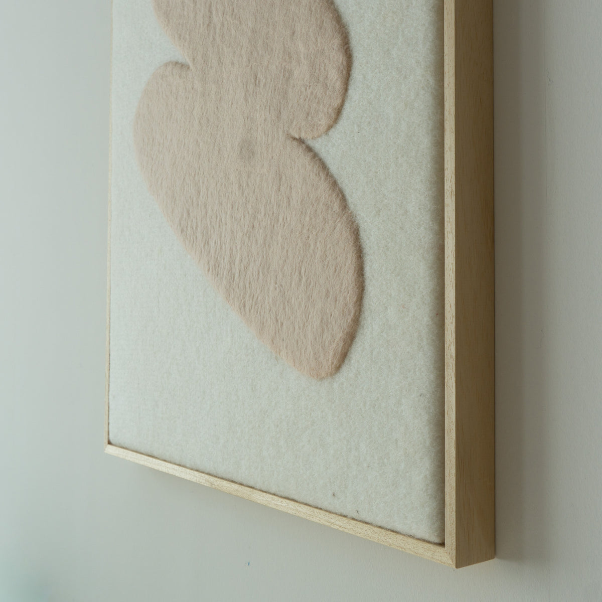 Close-up van het Stone wandkleed met beige wolvorm op een lichte vilten ondergrond.